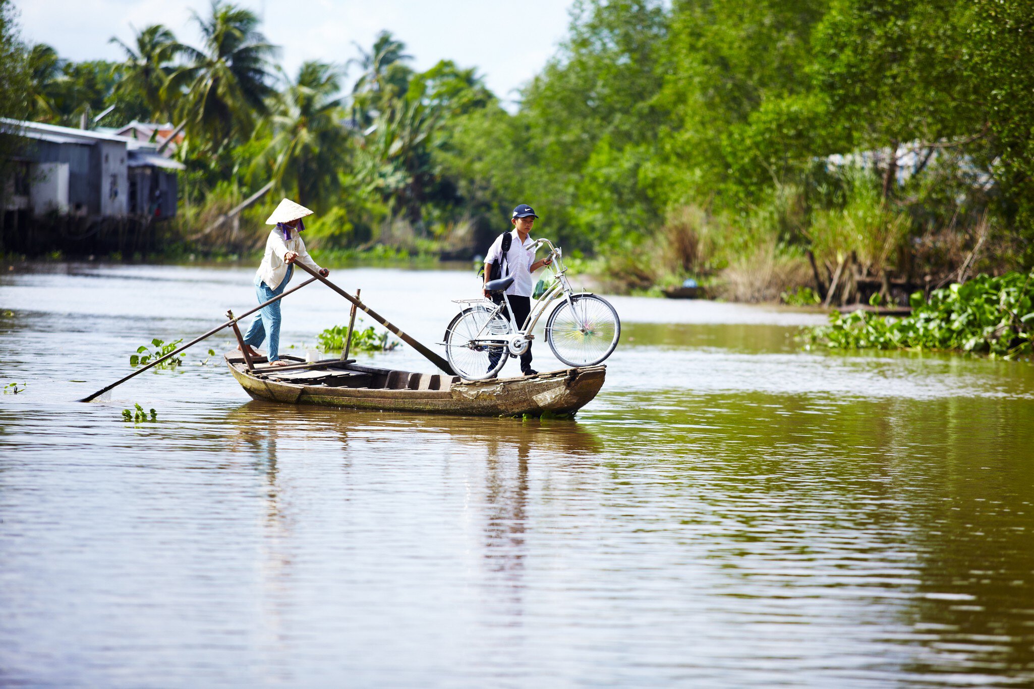 Boy using boat to transport bicycle across river.