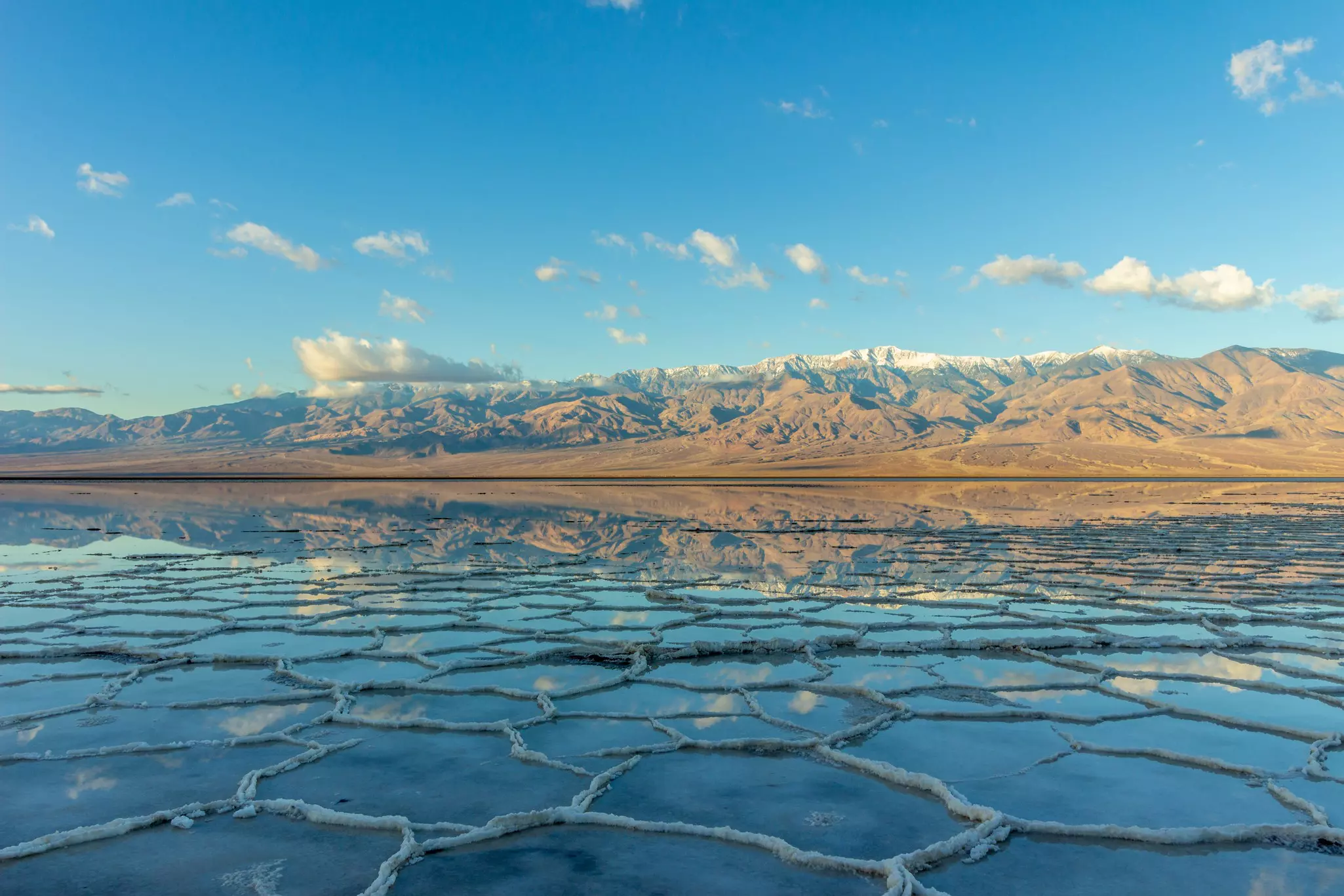 Salt flats with a layer of water reflecting the distant mountains like a lake