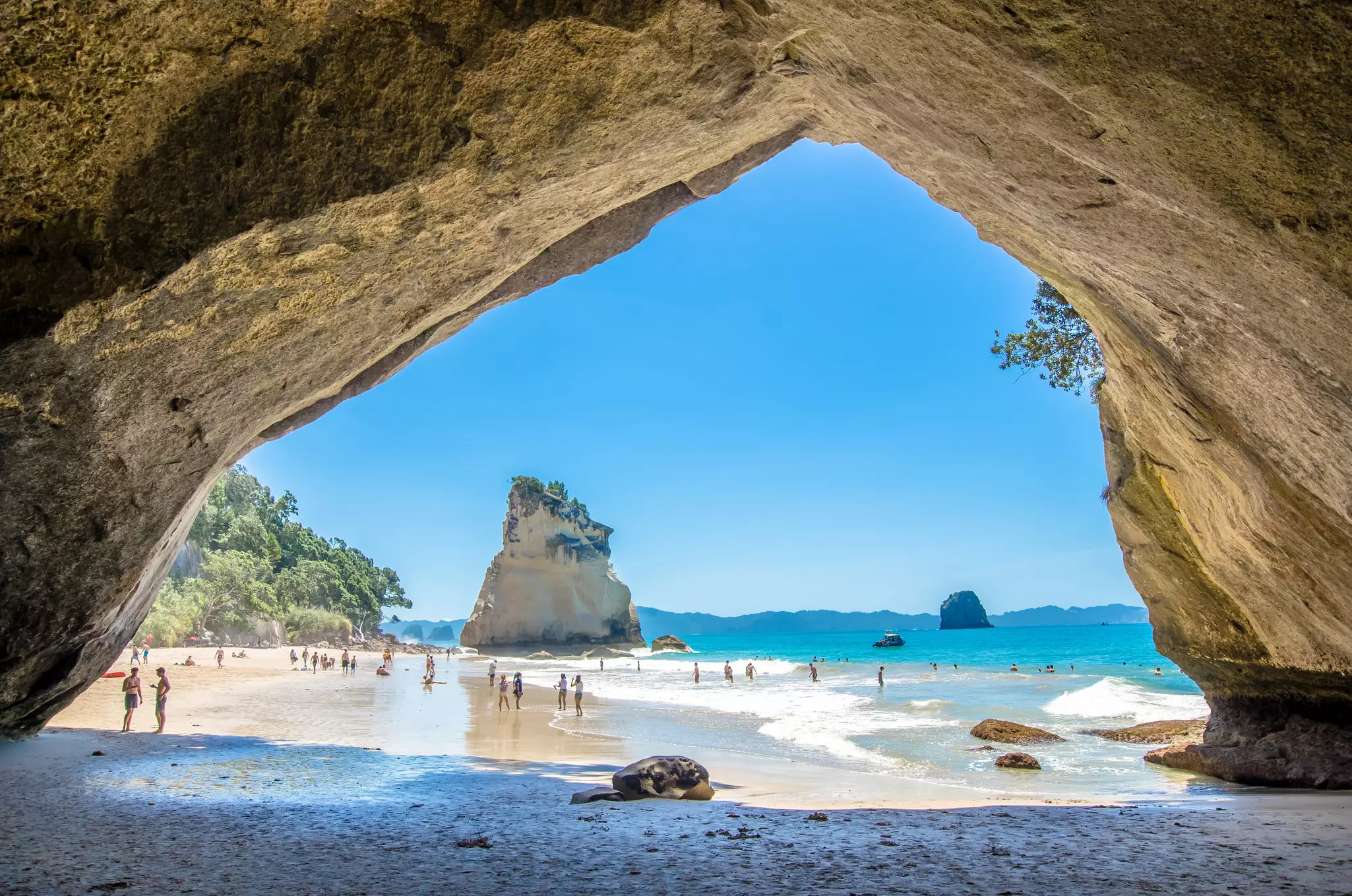 People on a sandy beach and swimming in the turquoise ocean in the shadow of a large freestanding rock