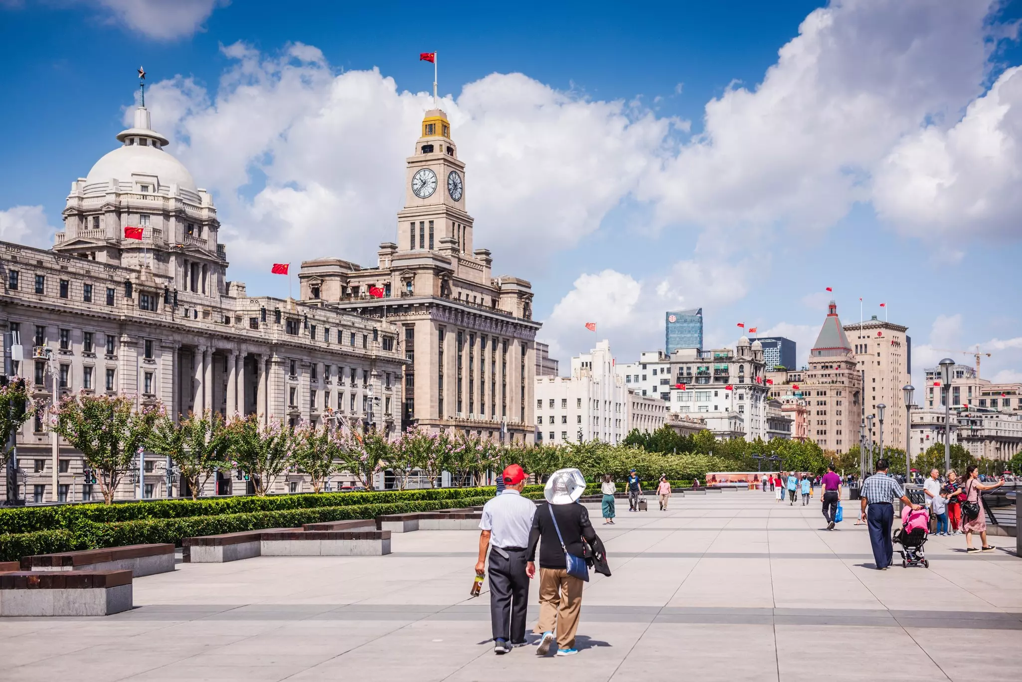 Pedestrians strolling along the Bund, a waterfront promenade lined with colonial-era buildings in Shanghai, China.