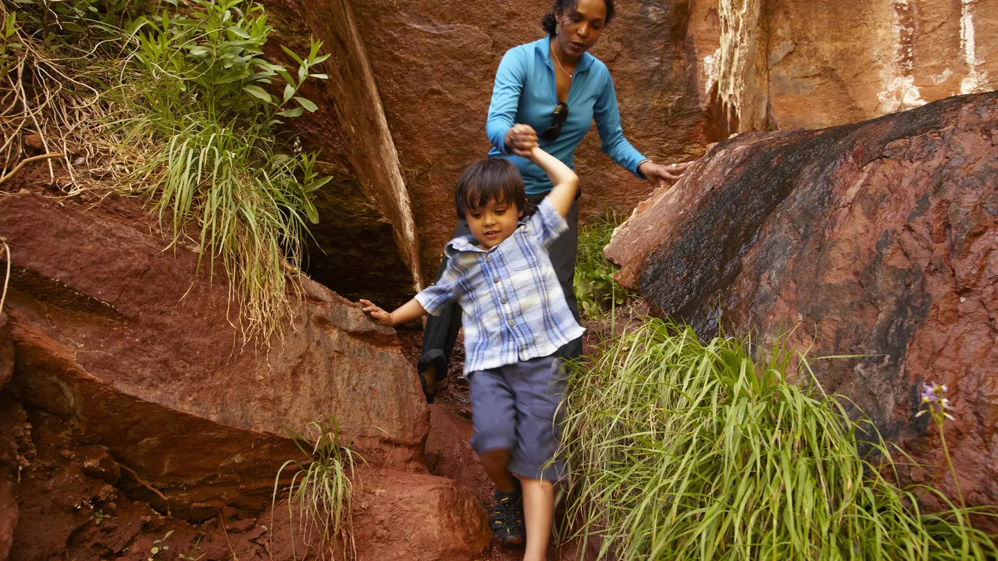 Mother helping son climb down rocks
