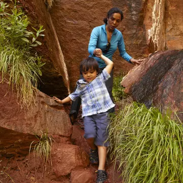 Mother helping son climb down rocks