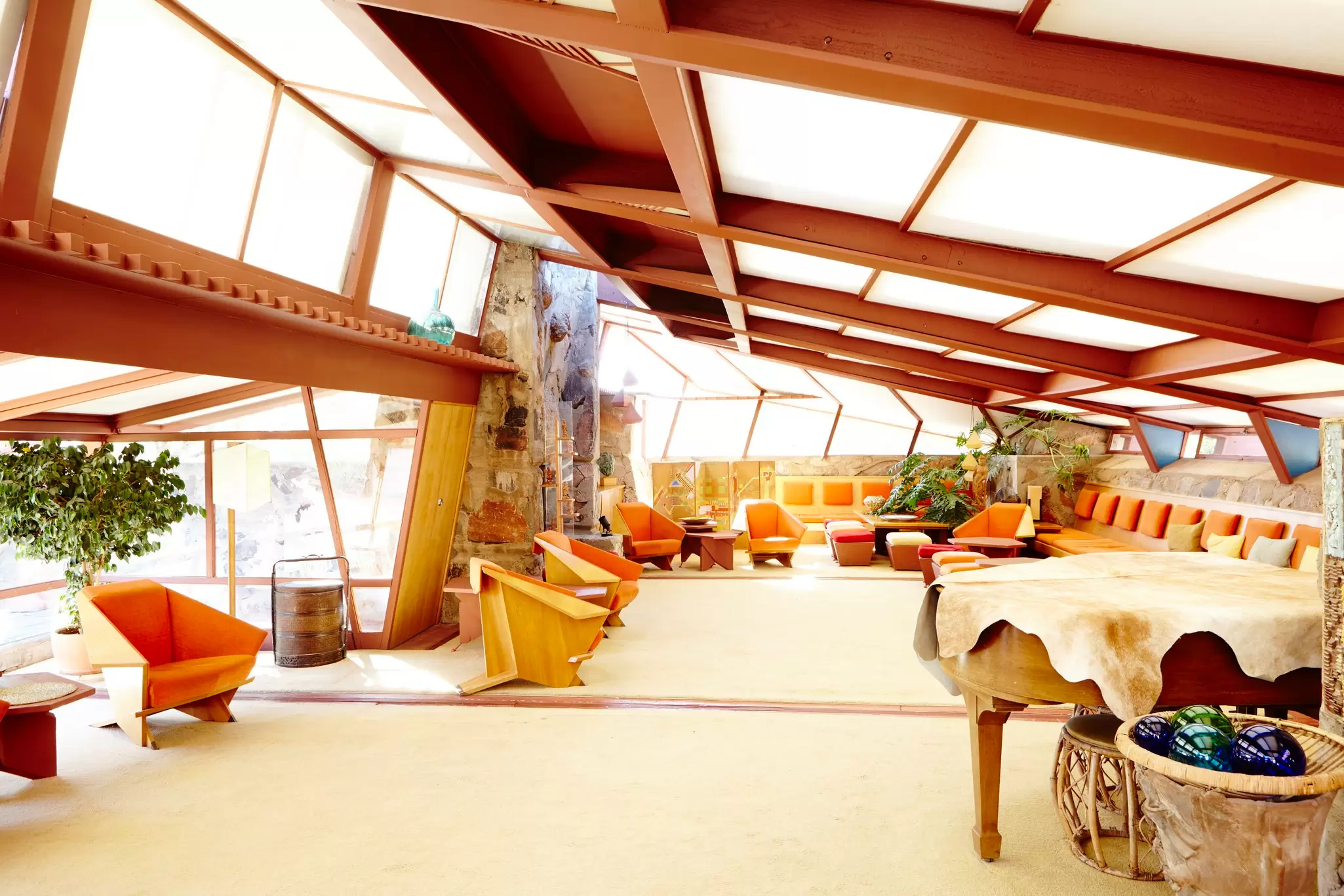 Organic mid-century interior with angular wood origami chairs, red steel beams and translucent sloping skylights