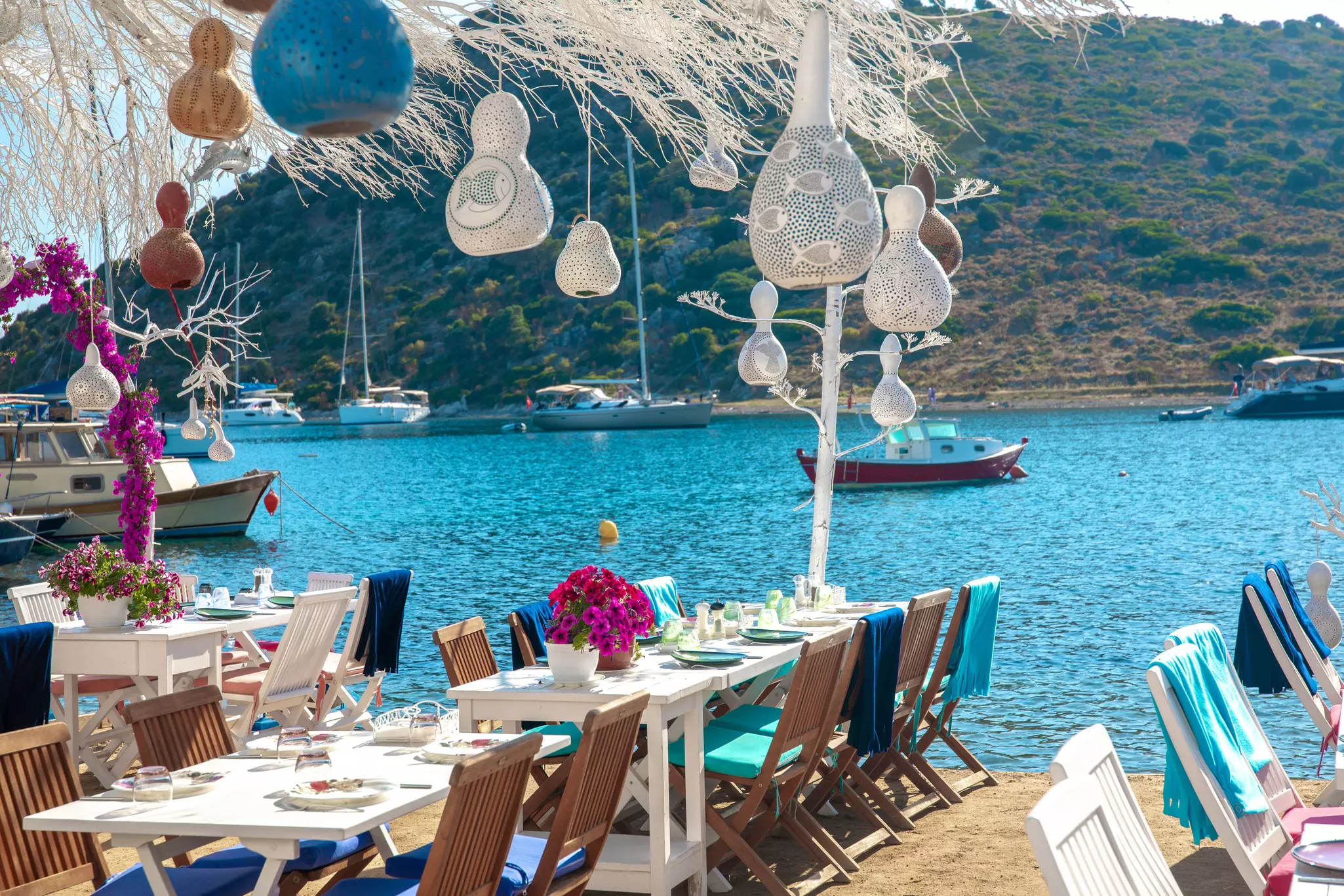 Festive outdoor dining scene with table and chairs, bougainvillea and hanging decorations on beach in Bodrum