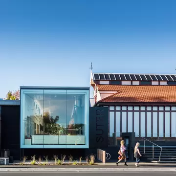 Exterior of Suter Art Gallery in Nelson, New Zealand. Pedestrians walking in front, blue sky above.