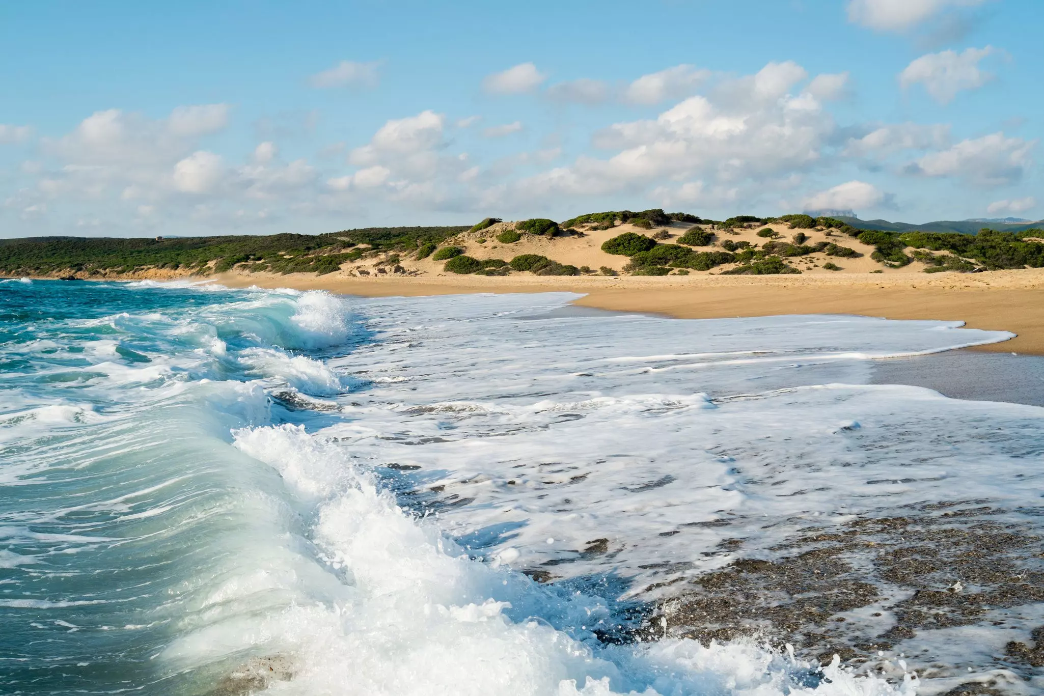 A beach, backed by tall sand dunes, is lapped by the ocean