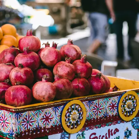  Ripe pomegranates in a brightly colored bin at an outdoor market.