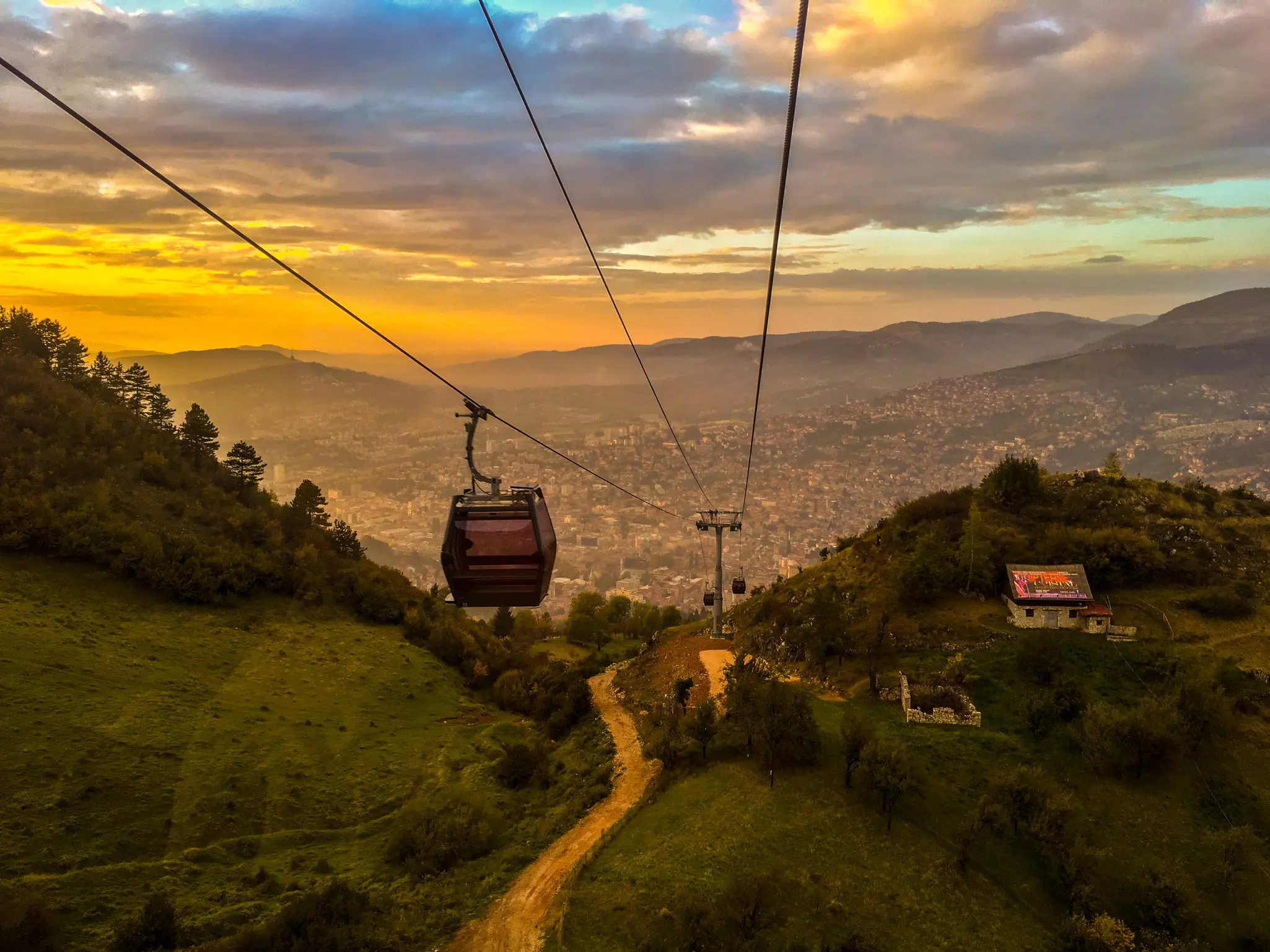 Gondolas on a cable car traveling between a city and a mountain at sunset.