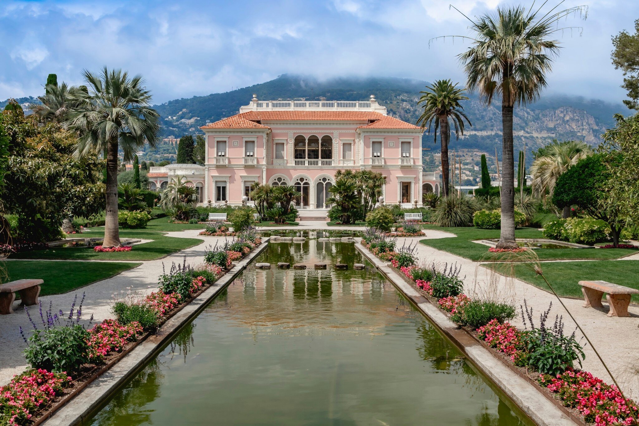 Villa Ephrussi de Rothschild in Saint-Jean-Cap-Ferrat, France. French Riviera. Beautiful gardens and a tranquil water feature set against scenic mountains.