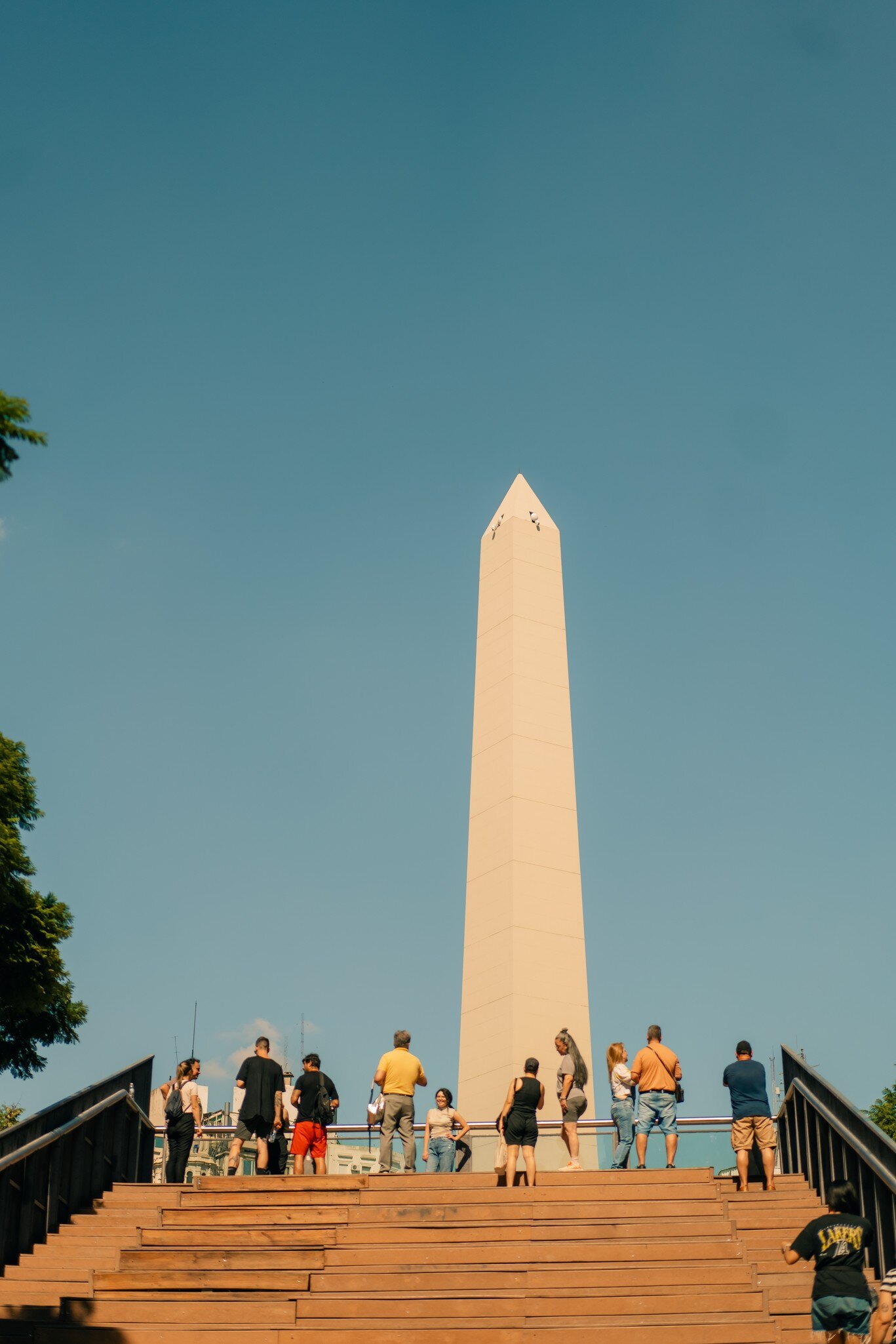 A group of people below the Obelisk (Obelisco) a major touristic destination in Buenos Aires, Argentina. Blue sky.