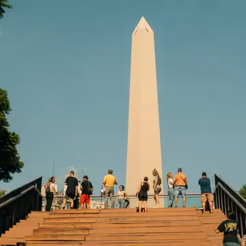 A group of people below the Obelisk (Obelisco) a major touristic destination in Buenos Aires, Argentina. Blue sky.