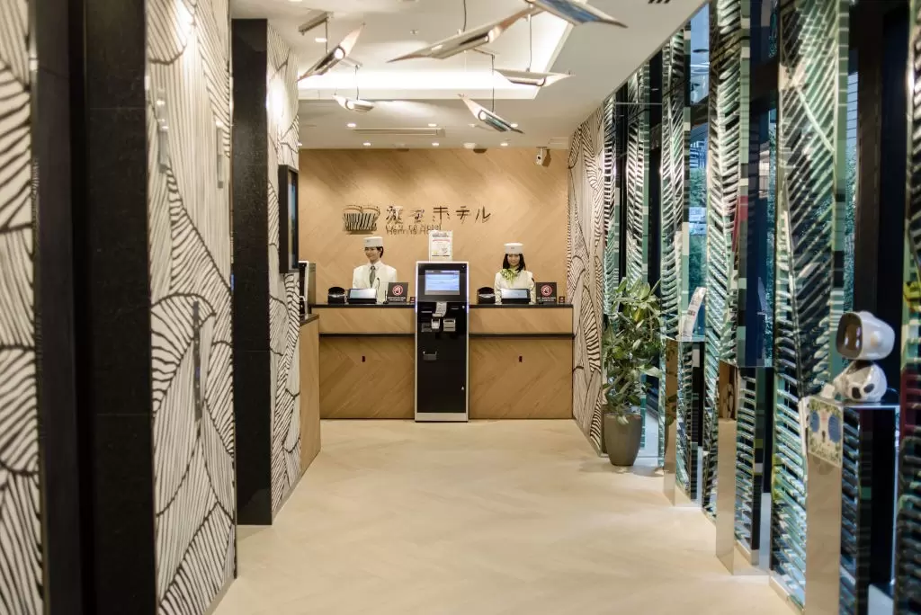 The bright reception area of a hotel in Tokyo, with two humanoid robots behind the desk with an ATM-like machine facing the guests