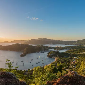 A boat moored in turquoise water by a sandy beach in Puerto Rico; the hillside is covered with green vegetation, and the sky is blue with white clouds.