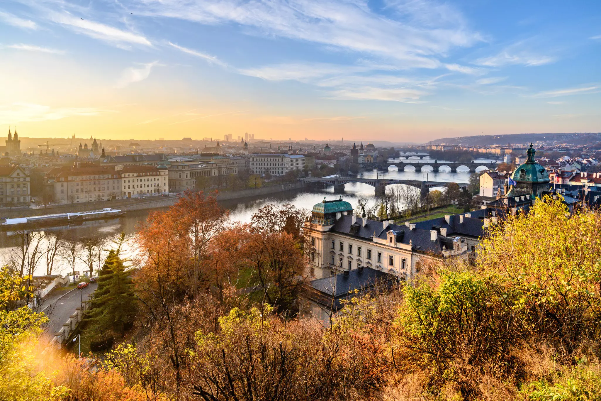 An autumn cityscape on either side of a river crossed by low bridges.