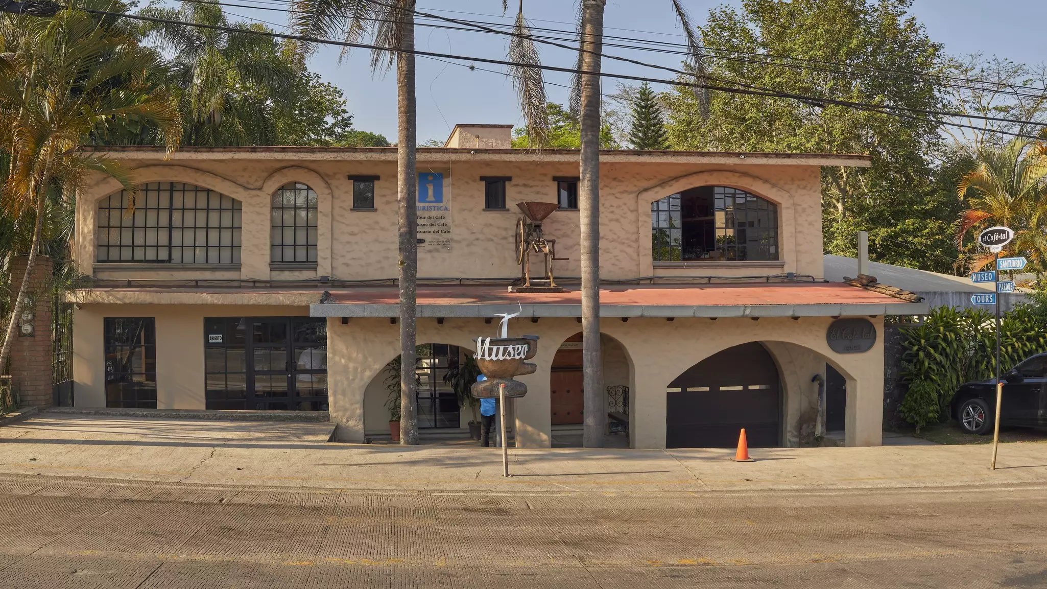 The facade of a low tan building with "Museo" on large sign shaped like a coffee cup on a sunny day.