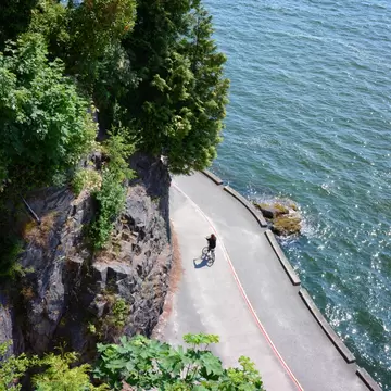 Cyclist rides on Stanley Park's famous Seawall on a sunny summer day in Vancouver, Canada.