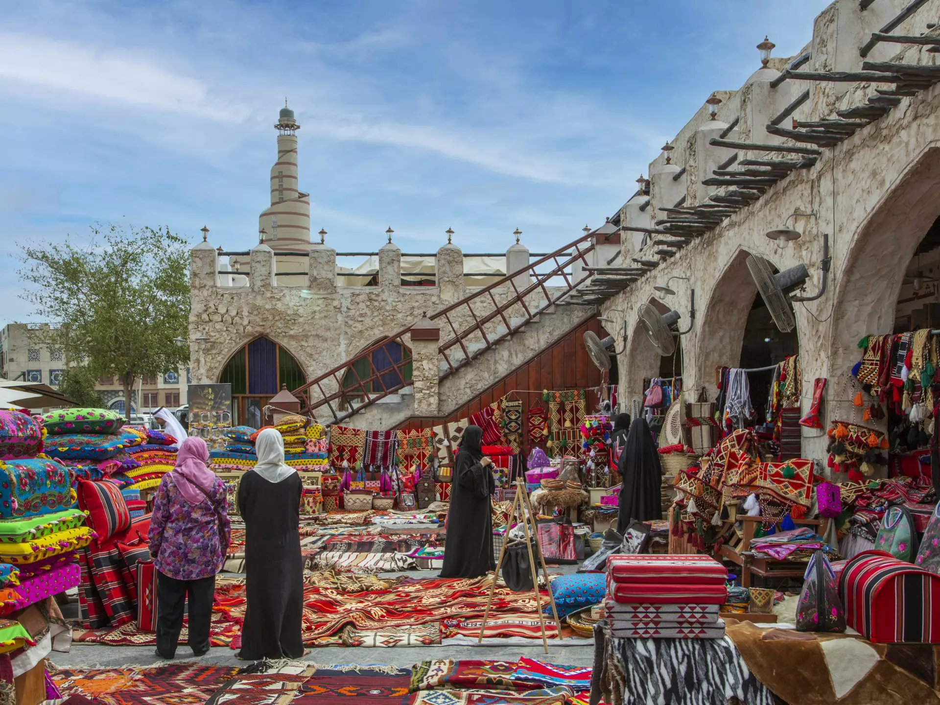 Carpets on sale in old Doha night souk, with Al-Fanar Qatar Islamic Cultural Center in the background.