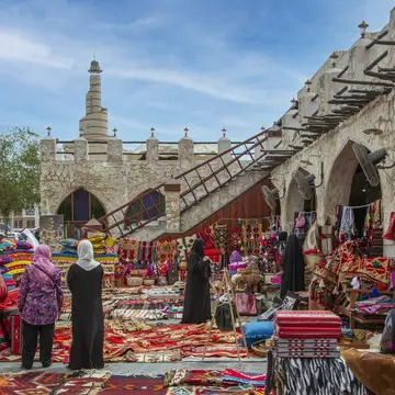 Carpets on sale in old Doha night souk, with Al-Fanar Qatar Islamic Cultural Center in the background.