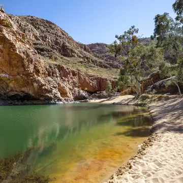 A blue-green waterhole lined by a white-sand beach