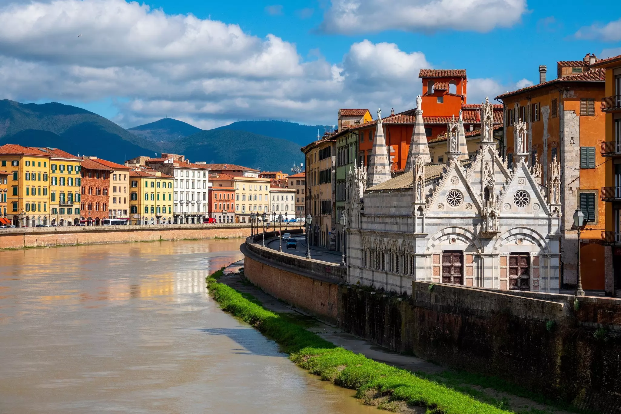 A small church stands next to a river in a city.