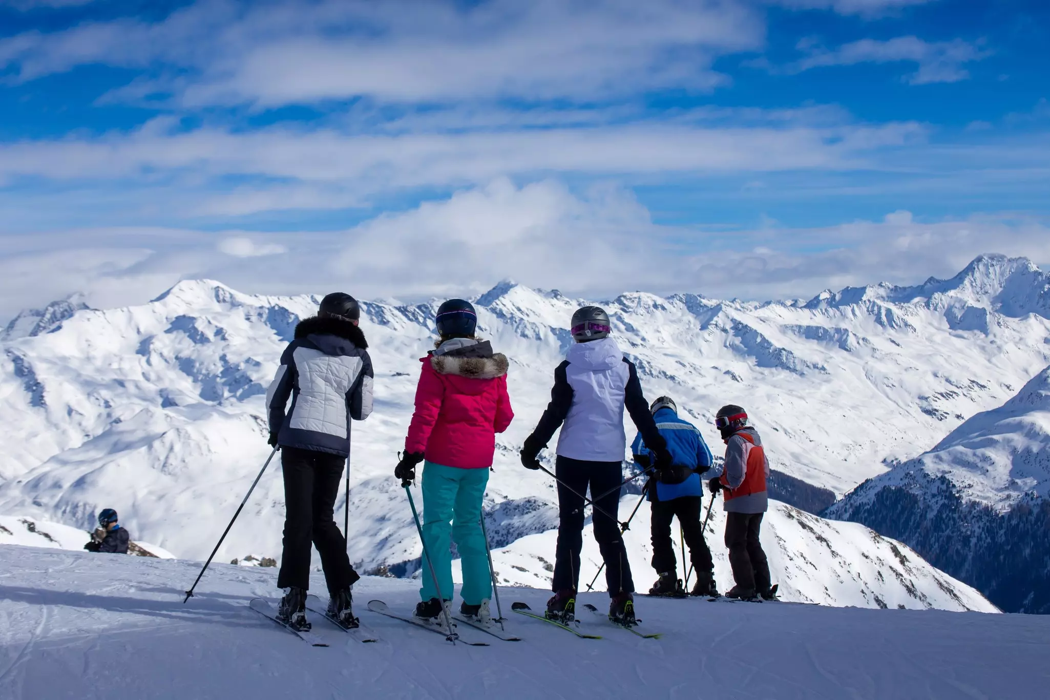 Five skiers look at a snow-covered mountain range from the top of a run in Switzerland.