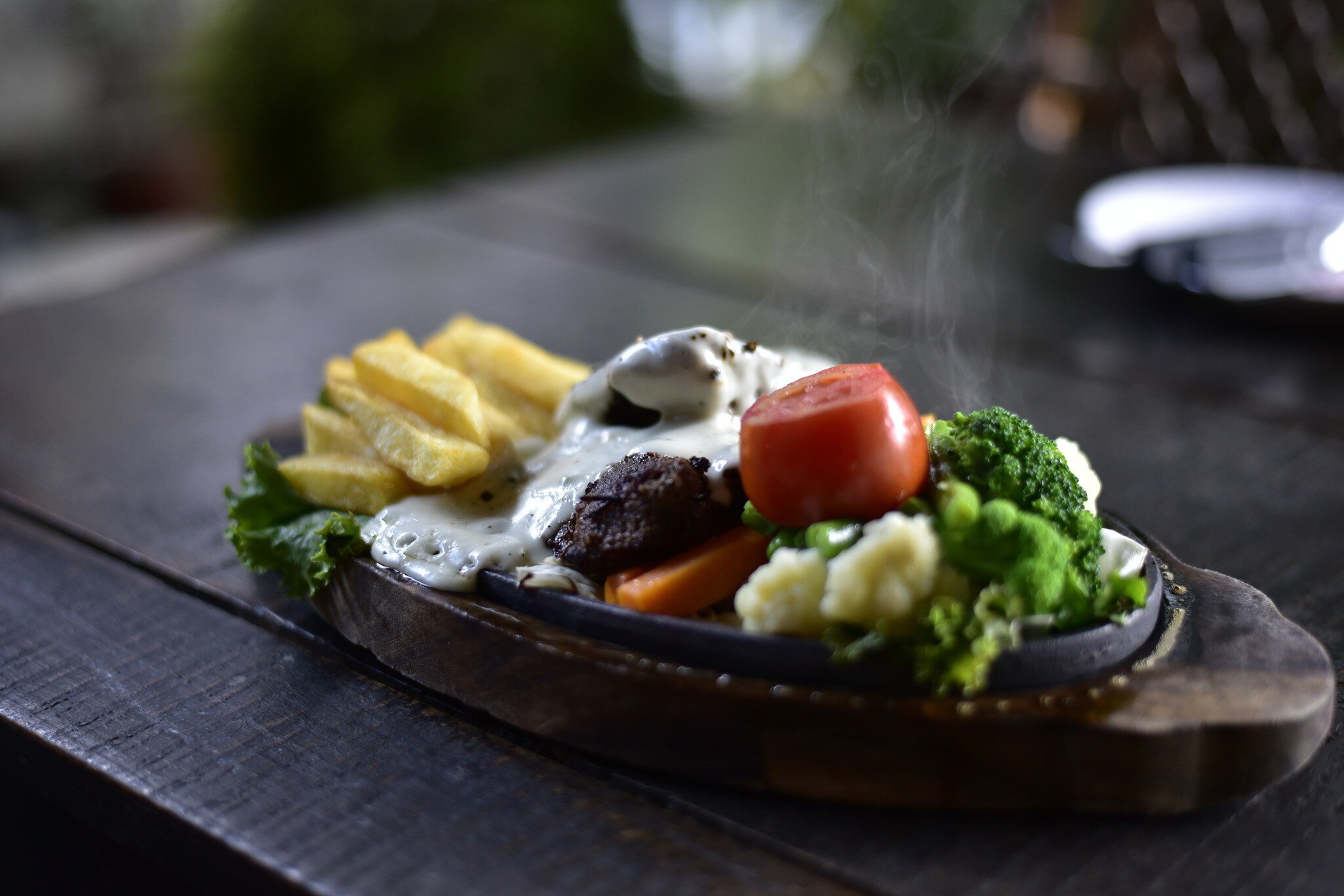 Appetizer; Backgrounds; Cheese; Close-up; Cooked; Cooking; Crockery; Cultures; Dinner; Food; Food and Drink; Freshness; Fried; Gourmet; Healthy Eating; Herb; Horizontal; Lunch; Meal; Meat; Nepal; No People; Onion; Pepper - Seasoning; Photography; Plate; Restaurant; Roast Dinner; Roasted; Savory Food; Savory Sauce; Sizzler; Spice; Tomato; Vegetable; Vegetarian Food; Wood - Material;
A hot plate BBQ steak sizzler with pepper cheese sauce, tomato, broccoli, and french fries, served in Pokhara.