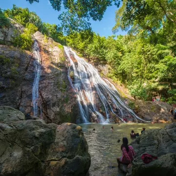 Na Muang Waterfall at Ko Samui Island, Thailand. Wide-angle with people swimming and sitting on rocks.