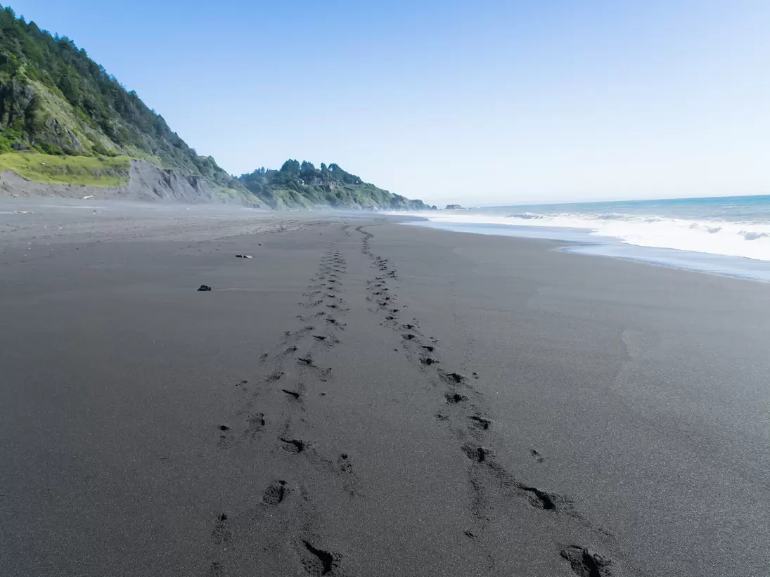 Footsteps in the black sand of the Lost Coast backpacking trail in California.