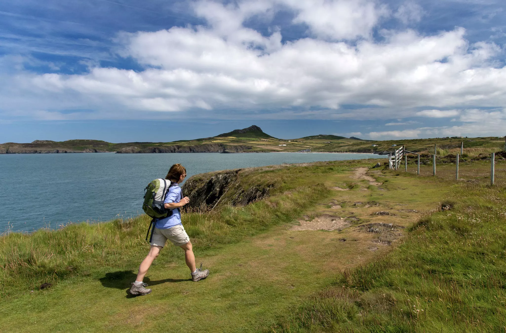 A hiker walking along the Pembrokeshire Coast Path on a sunny day with a view of cliffs and sea.