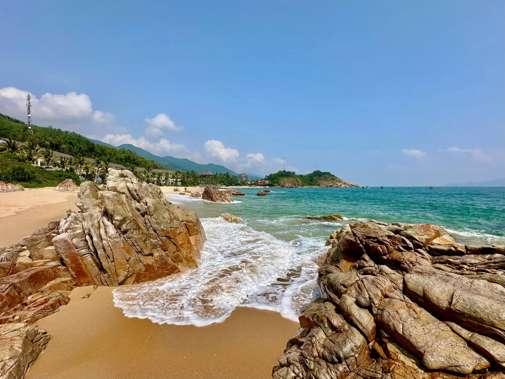 A golden-sand stretch of beach dotted with large rocks.