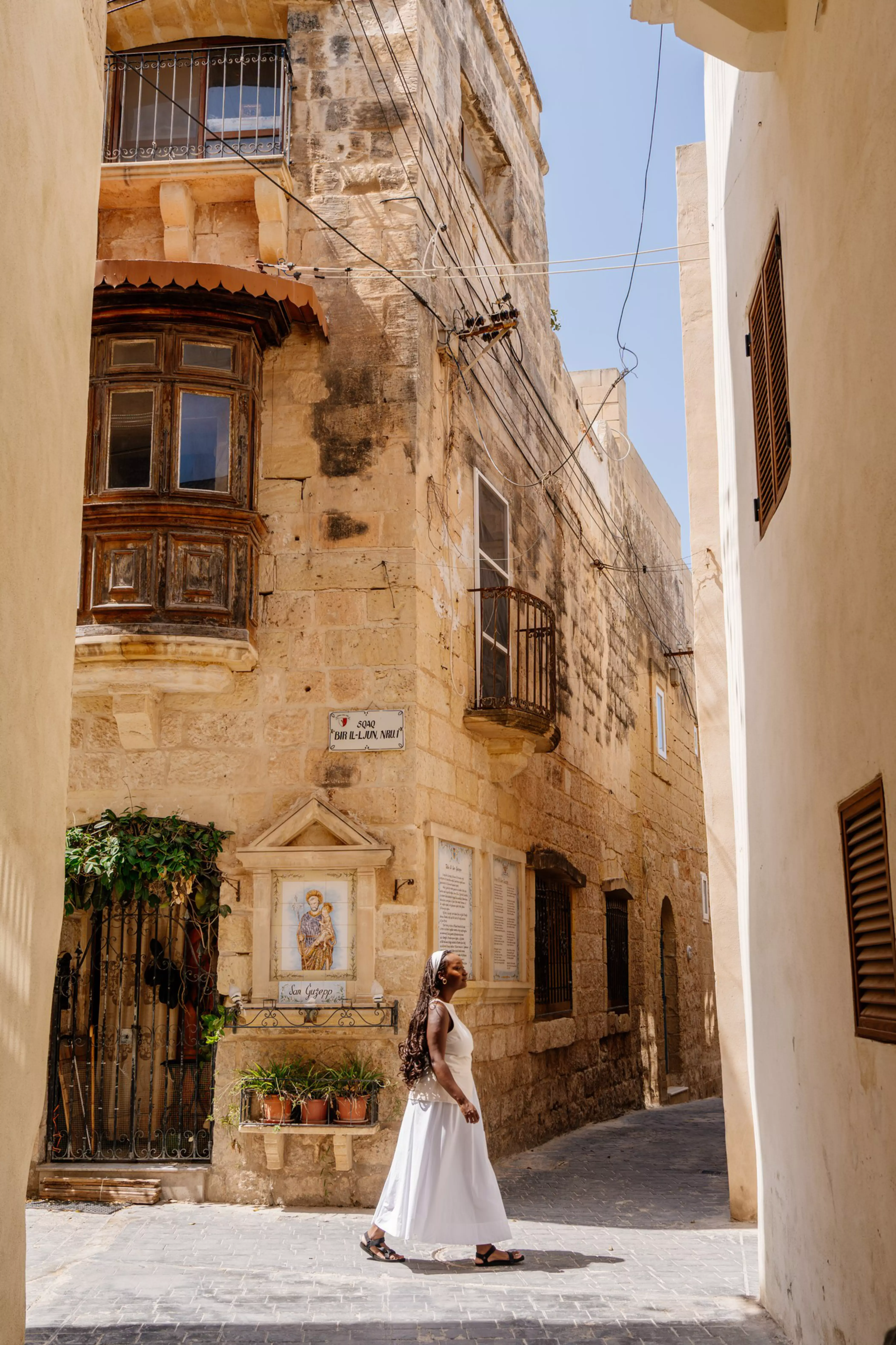 Jacklynn walking through a narrow stone street in Malta, surrounded by historic buildings and balconies.