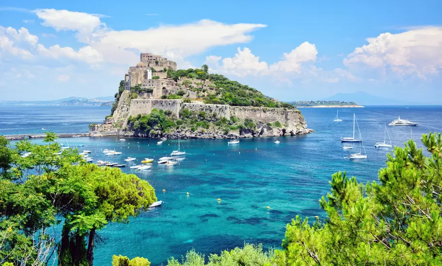 Castello Aragonese fortress on a rocky islet off Ischia, linked by a causeway, with boats moored in turquoise water