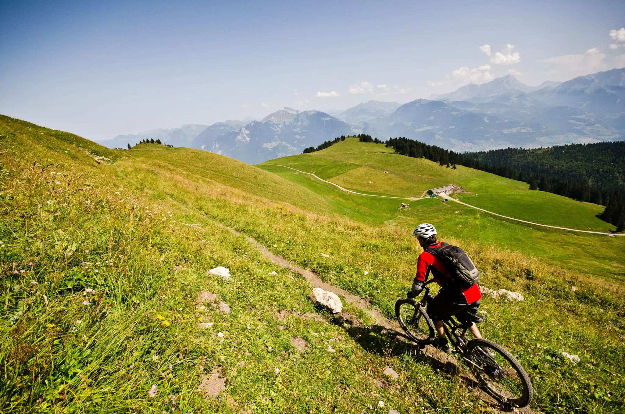 A mountain biker riding a narrow single-track along a green valley in the Portes Du Soleil region of the Alps