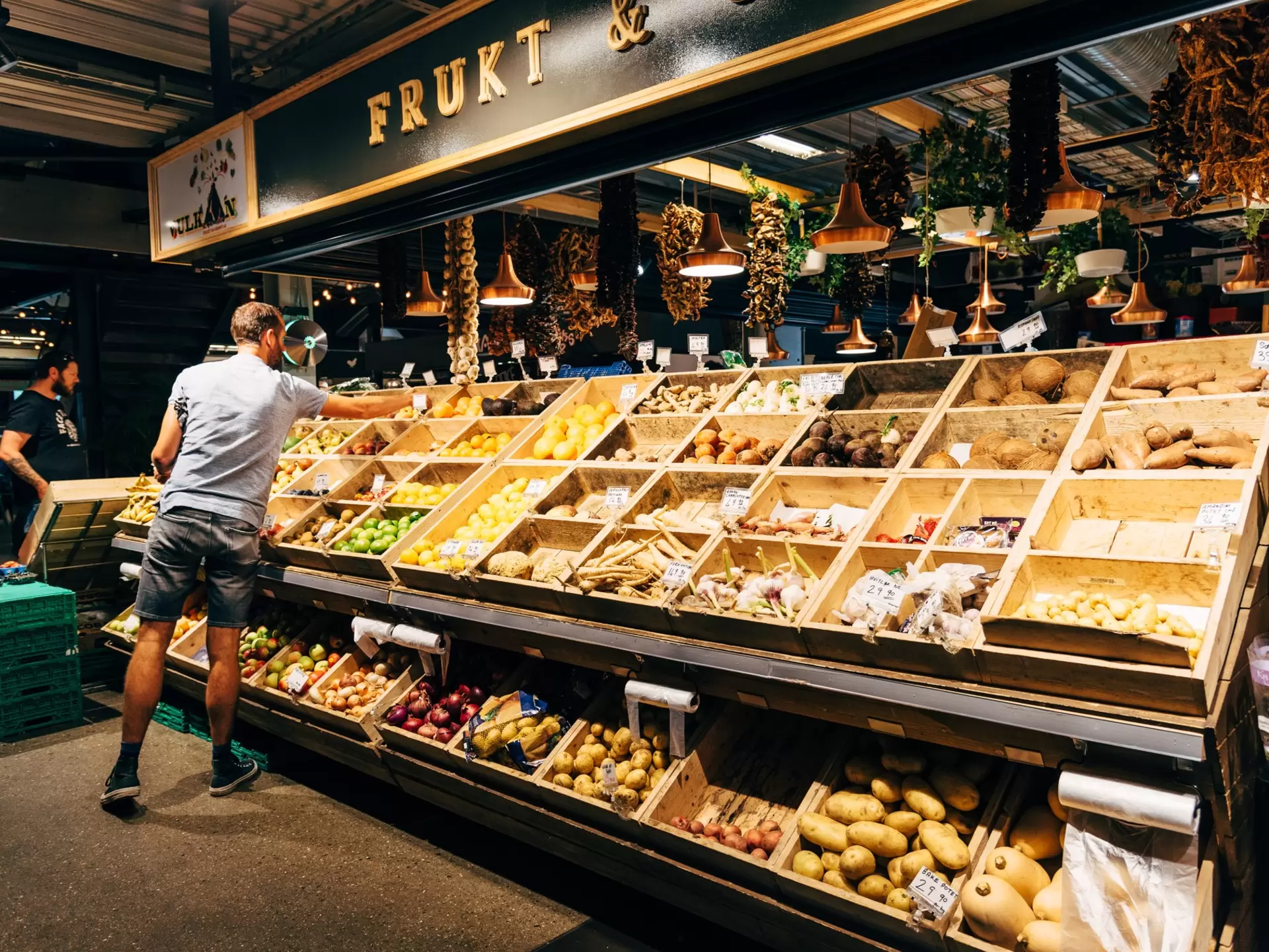 A man shops for fresh produce from wooden bins in a local market in Oslo, Norway.