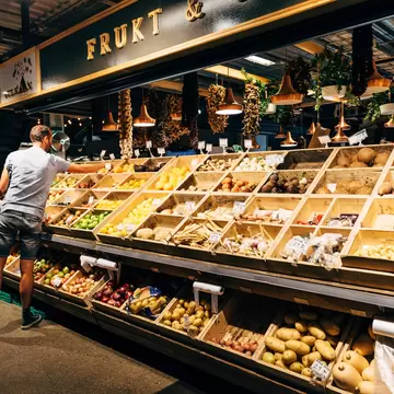 A man shops for fresh produce from wooden bins in a local market in Oslo, Norway.