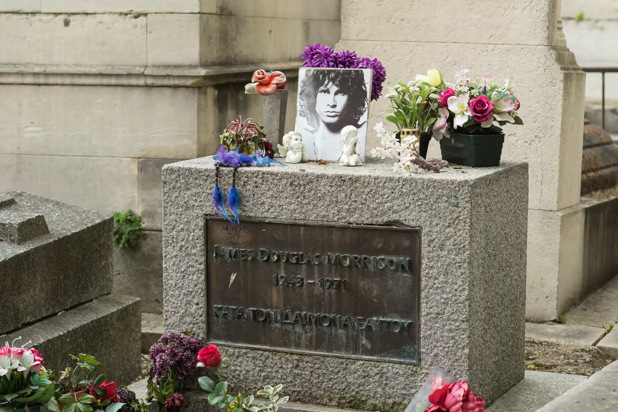 Several bouquets of flowers and a picture of Jim Morrison on his gravestone in the Pere Lachaise Cemetery.