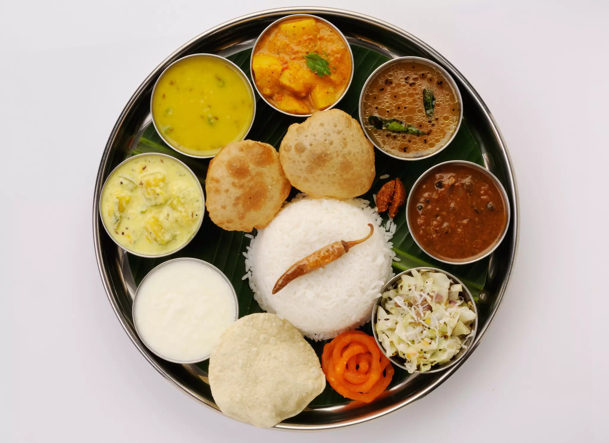 Traditional vegetarian Indian thali lunch with rice, vegetables and sauces in small containers on a circular platter