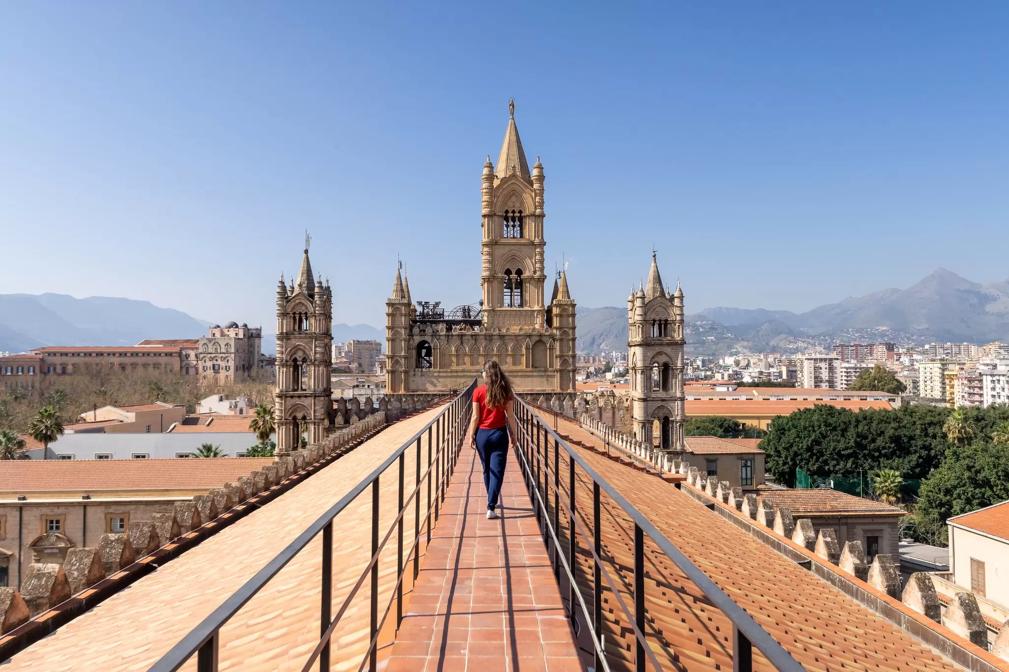 Female tourist visitor walking on the rooftop catwalk of the Palermo Cathedral or Cattedrale di Palermo with bell towers in the background on a nice sunny afternoon in Palermo.