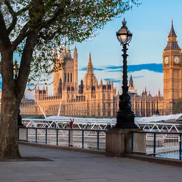 An ornate building with many towers, including a very tall clock tower, by a river.