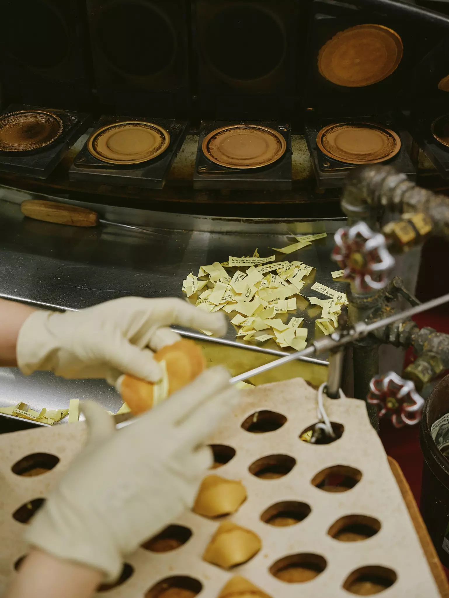 Gloved hands assembling a fortune cookie. A small pile of fortunes is in the background