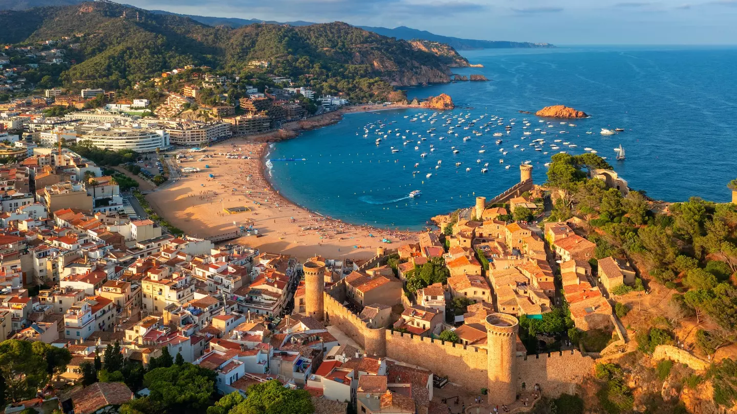 A c-shaped sandy bay, surrounded by forests, cliffs, whitewashed buildings and a medieval castle.