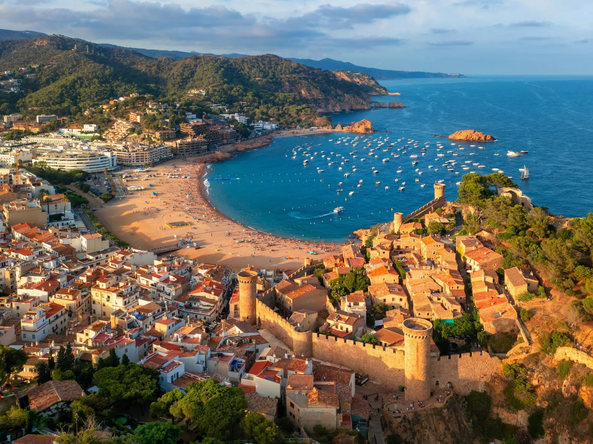 A c-shaped sandy bay, surrounded by forests, cliffs, whitewashed buildings and a medieval castle.