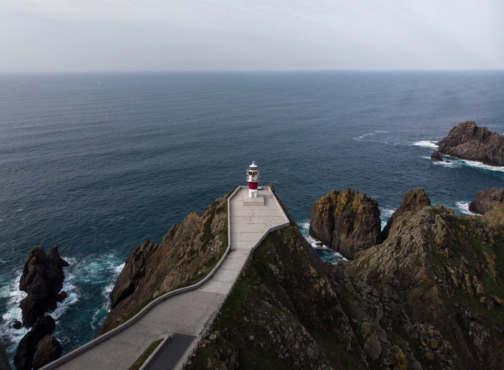 Aerial view of the Cabo Ortegal lighthouse on a steep rocky cliff in Galicia, Spain, with the sea in the background.