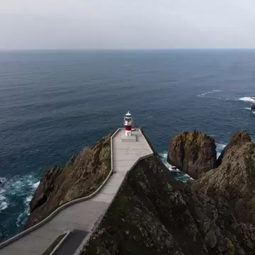 Aerial view of the Cabo Ortegal lighthouse on a steep rocky cliff in Galicia, Spain, with the sea in the background.
