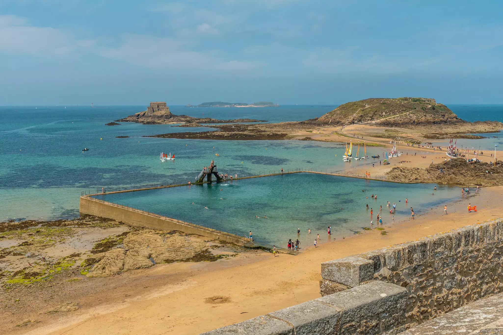 People swim in a pool fed by the sea at the edge of a sandy beach