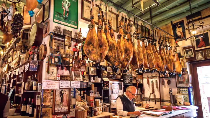 Barman behind bar of old-school tapas bar with ham joints hanging from ceiling