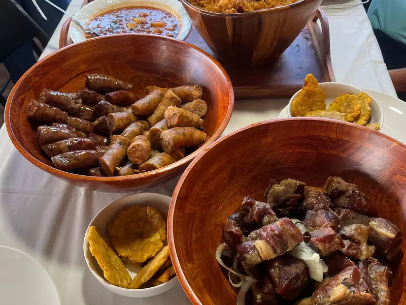 A table set with large wooden bowls filled with sausages, roasted pork, and rice and beans, and smaller bowls with tostones.