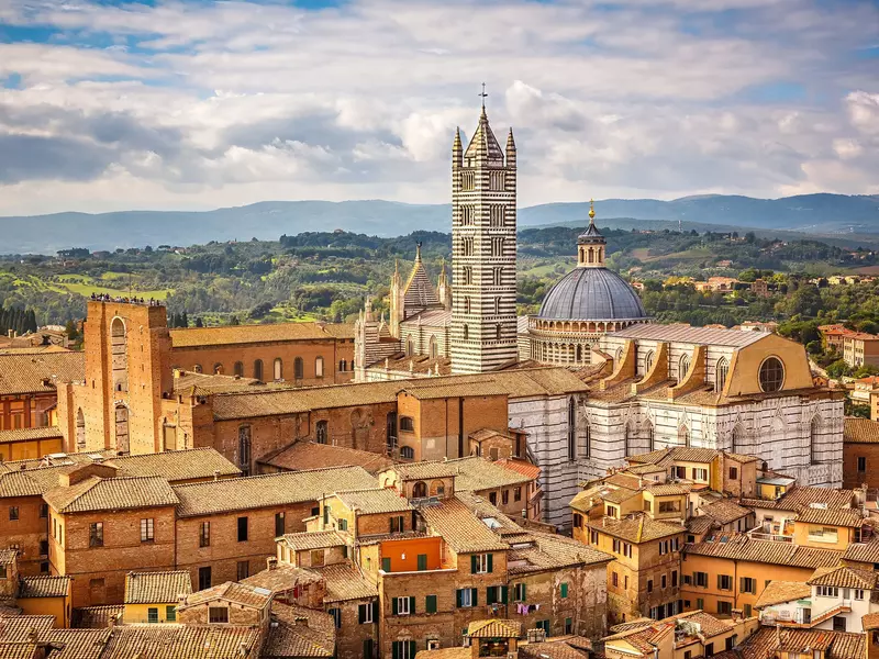 The red-stone buildings and ornate tower of a cathedral in Siena, Italy. 