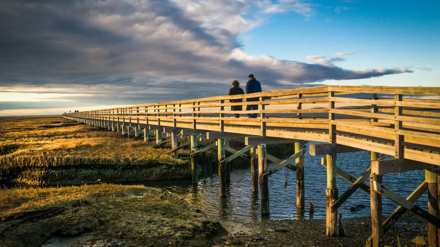 A couple walk along a boardwalk on a winter's day with the sun low in the sky