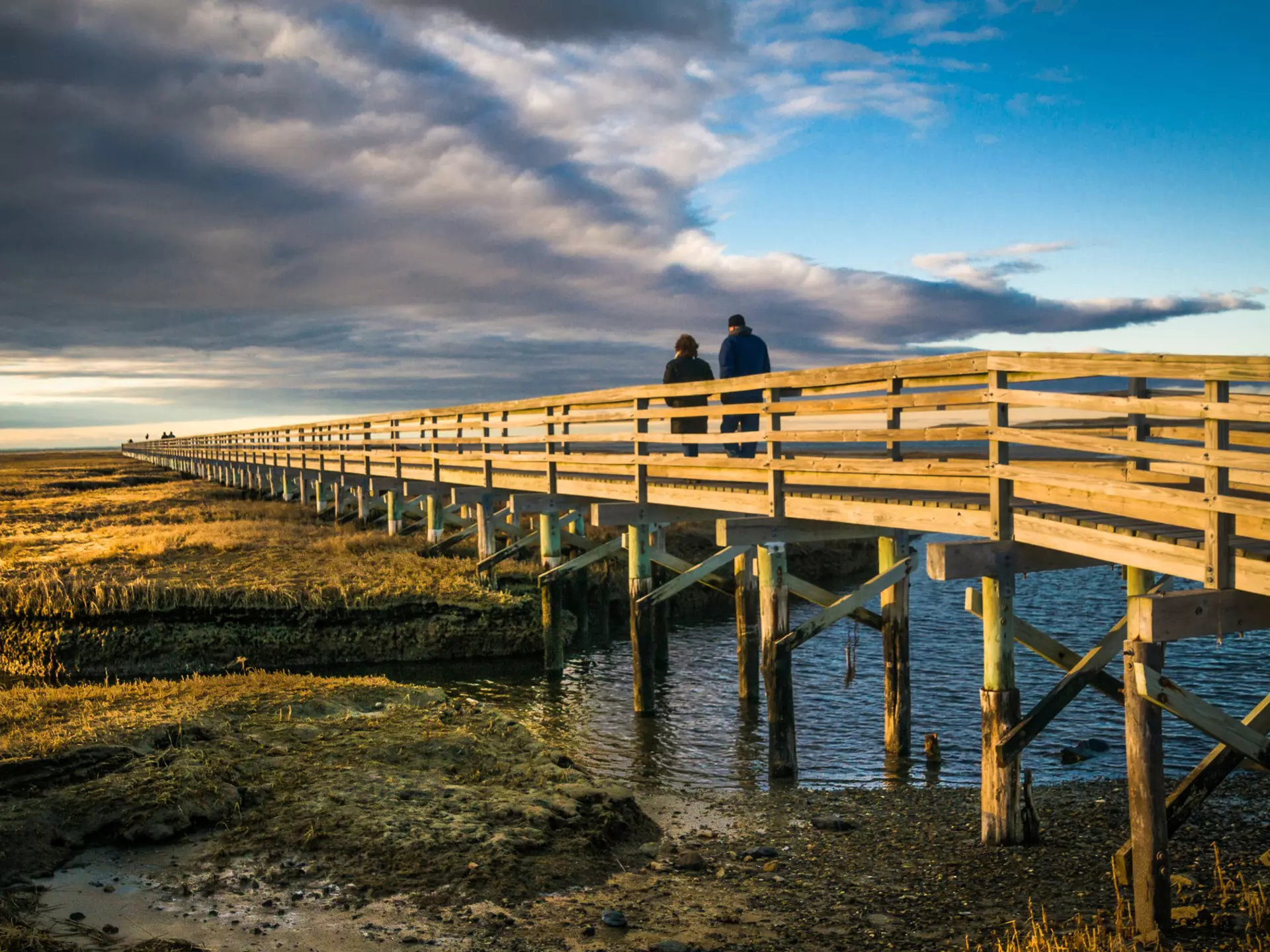 A couple walk along a boardwalk on a winter's day with the sun low in the sky